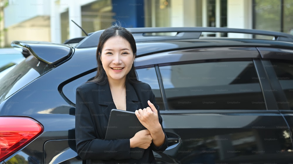Attractive businesswoman is standing near her car and smiling to camera.