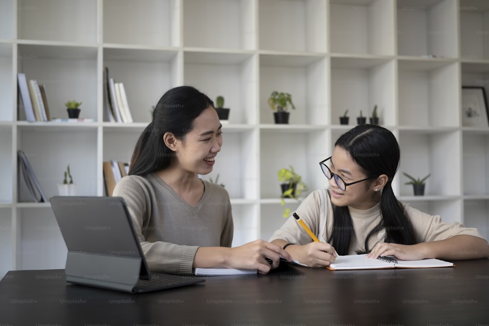 Smiling asian mother helping her daughter with homework at home.