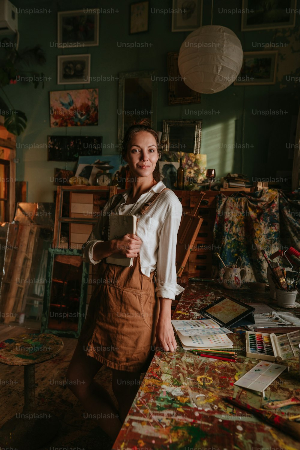 Portrait of young caucasian female artist with sketchbook at her cozy workshop. Selective focus.