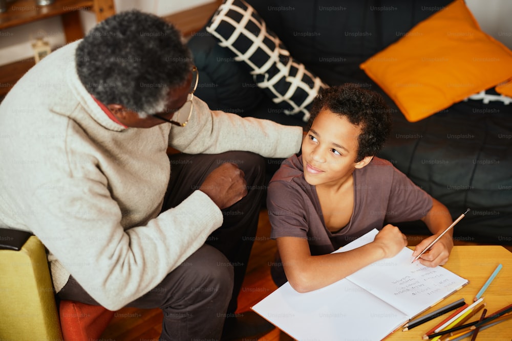 Ein afroamerikanischer Großvater sitzt zu Hause bei seinem Enkel und hilft ihm bei den Hausaufgaben.