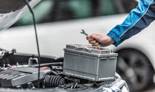 Mechanic holds key over car battery with engine trunk of the car open.