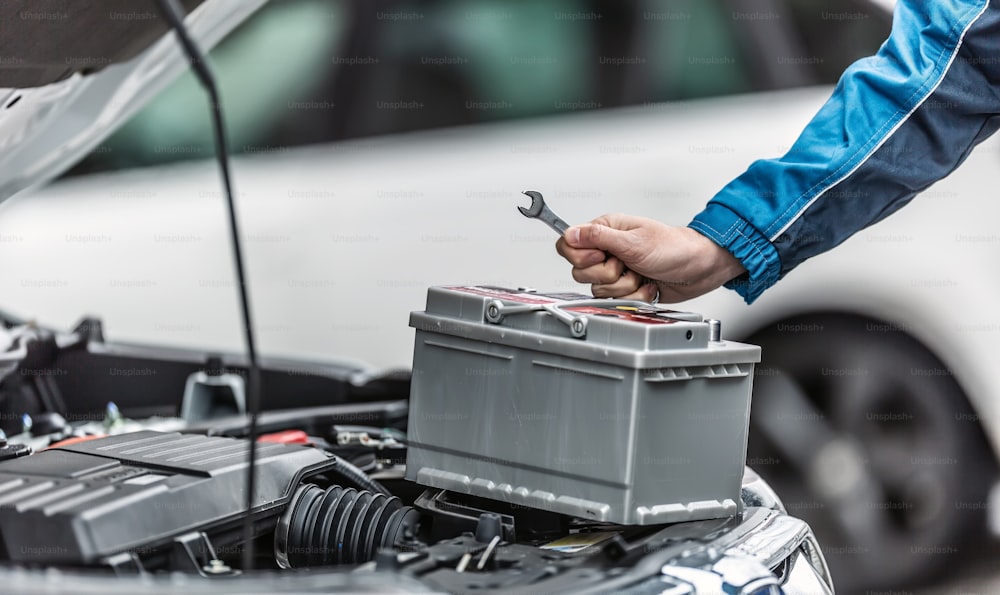 Mechanic holds key over car battery with engine trunk of the car open.