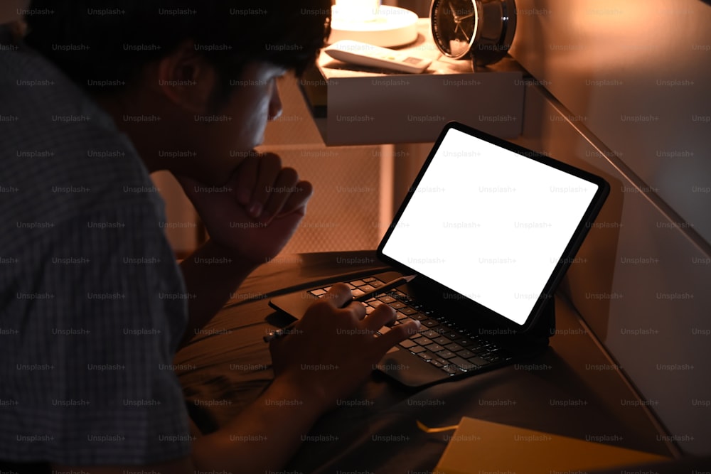 Junger Mann, der nachts ein digitales Tablet in seinem bequemen Bett benutzt.