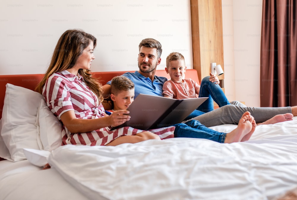 Family of four enjoying together at hotel room, sitting at bed reading hotels offers.
