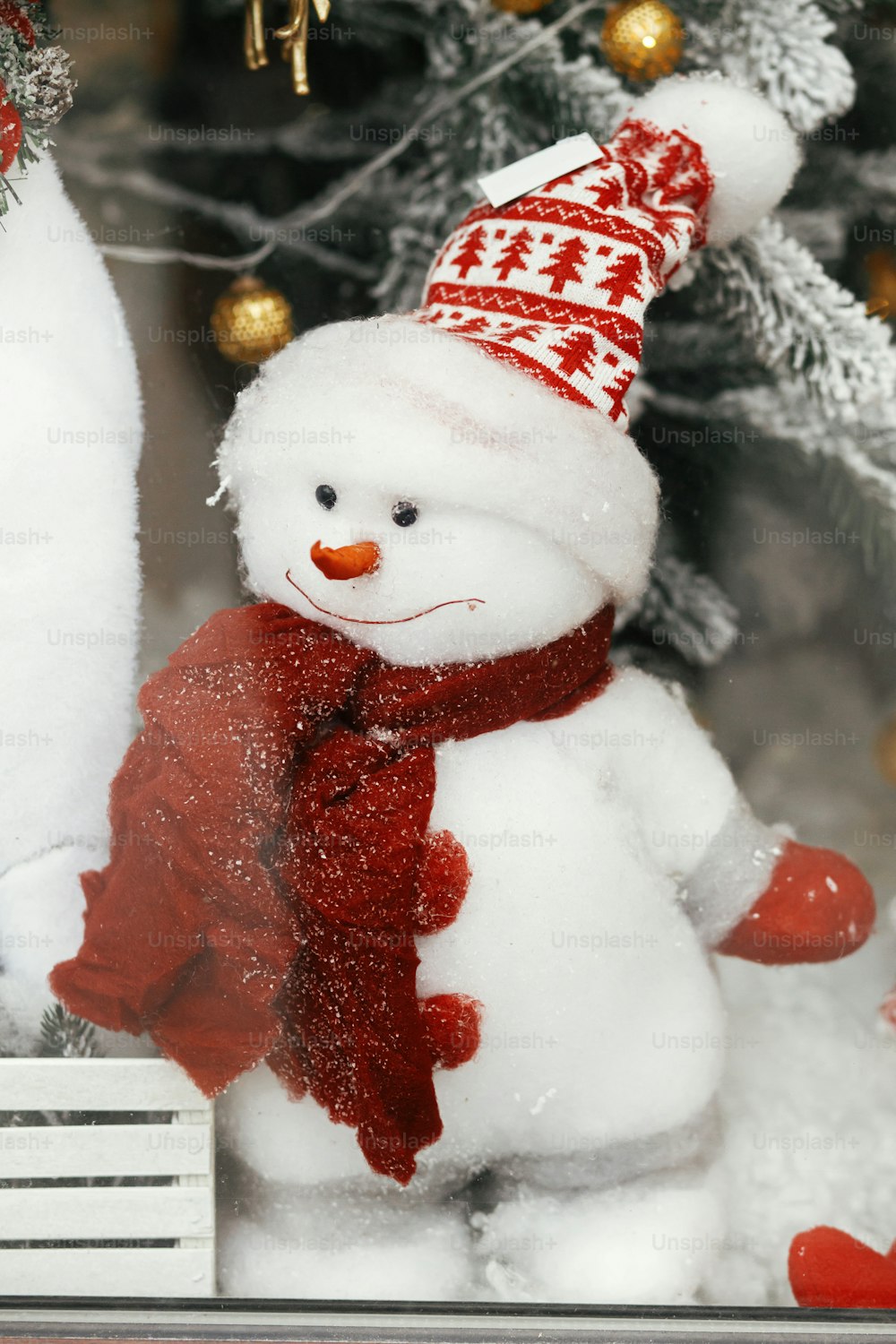 Stylish cute snowman in hat and with scarf toy under modern christmas tree. Christmas festive decor for winter holidays in european city street. Merry Christmas!