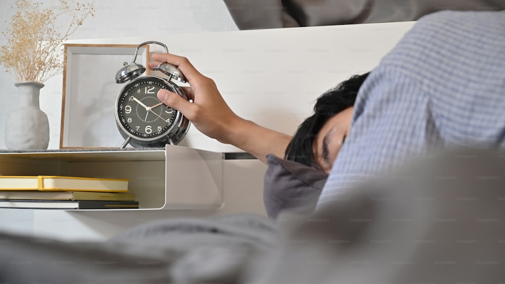 Man lying in bed and extend hand reaching to turn off alarm clock switch.