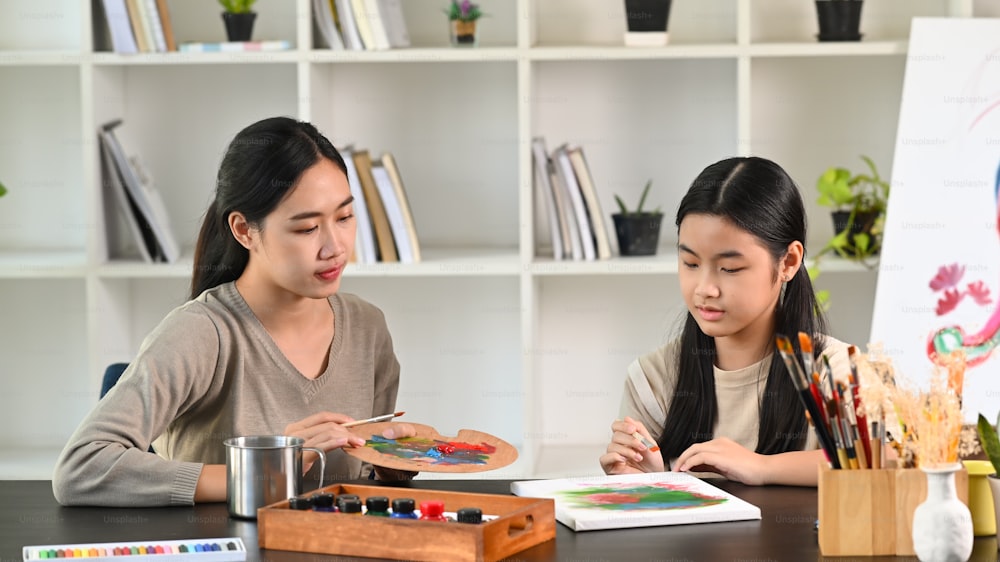 Schöne asiatische Mutter und Tochter malen zusammen im Wohnzimmer.