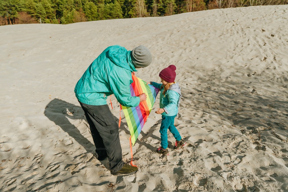 Dad and daughter having fun time on the sand beach with colorful kite. Happy family activities outdoor. Parenthood concept.