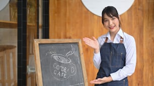 Friendly waiter standing with black board at the doorway of coffee shop.