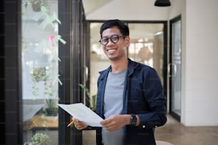 Young creative man standing in modern office and smiling to camera.