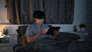 Asian man sitting in bedroom and browsing internet with digital tablet.