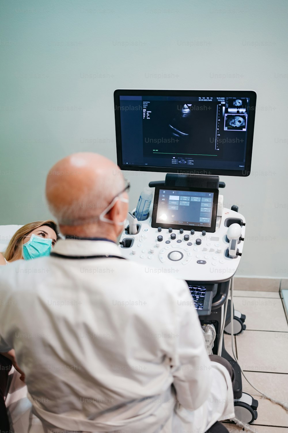 Experienced senior doctor performs a cardiac examination on a young female patient. He is using cardiology scanner. Medicine and modern technology concept.