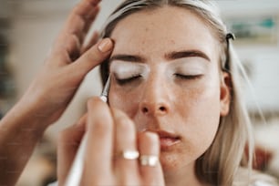 Close up shot of beautiful young woman face getting make-up. The artist is applying eyeshadow base with brush. Professional beautician work.