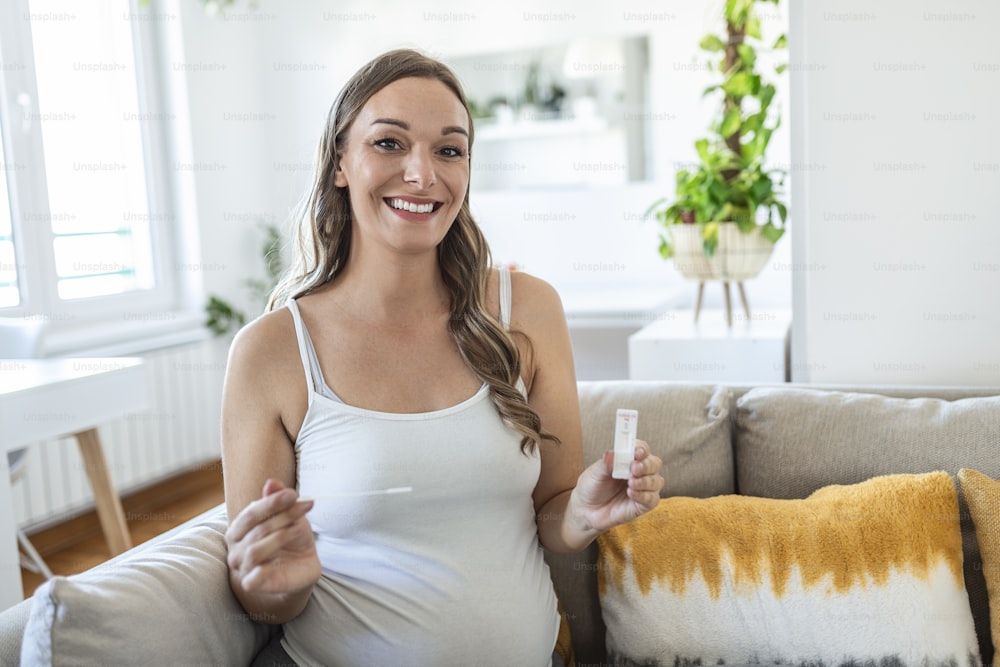 Primer plano de la mano de una mujer embarazada sosteniendo un dispositivo de prueba negativo. Mujer embarazada feliz mostrando su coronavirus negativo - Prueba rápida Covid-19. Coronavirus
