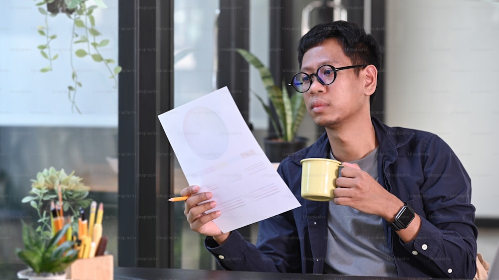 Designer creativo uomo asiatico che beve caffè e lavora con il campione di colore in ufficio.