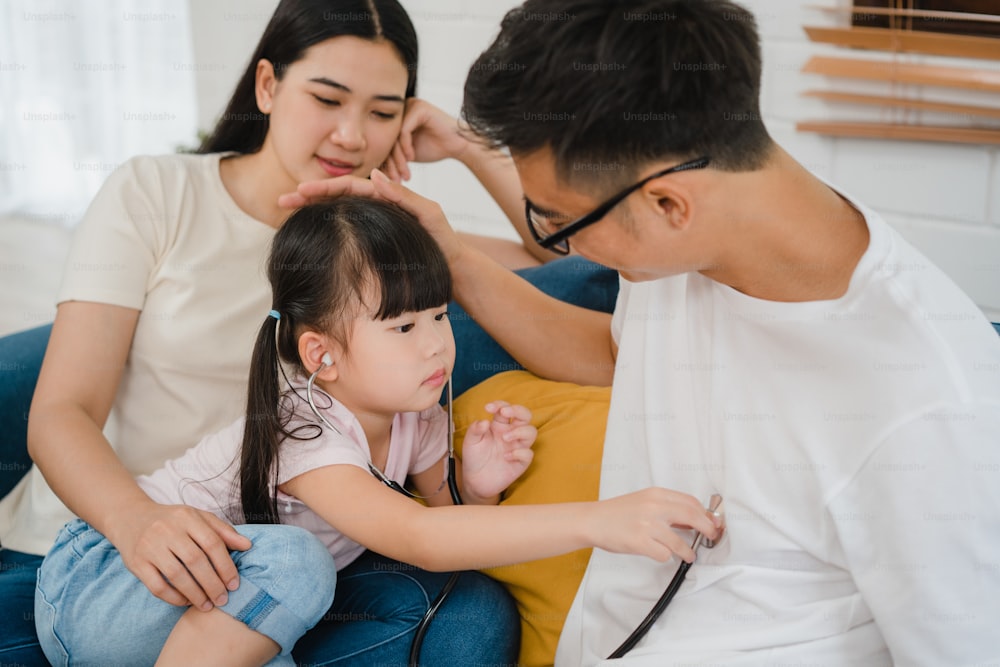 행복한 쾌활한 아시아 가족 아빠, 엄마, 딸은 집에서 소파에서 즐거운 시간을 보내는 의사로 재미있는 게임을 하고 있습니다.
