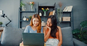 Asia lesbian women site on couch together looking at laptop screen in living room at home together. Happy couple roommate ladies enjoy web surfing online shopping, Lifestyle woman at home concept.