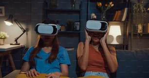 Attractive Asia ladies enjoy happy moment shopping online experience with virtual reality glasses headset site on couch living room in home at dark night.