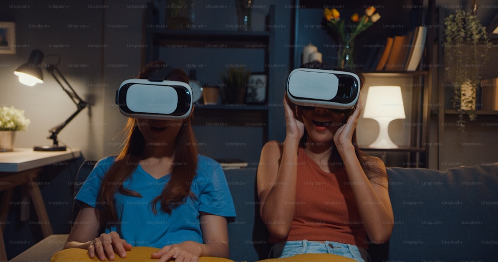 Attractive Asia ladies enjoy happy moment shopping online experience with virtual reality glasses headset site on couch living room in home at dark night.