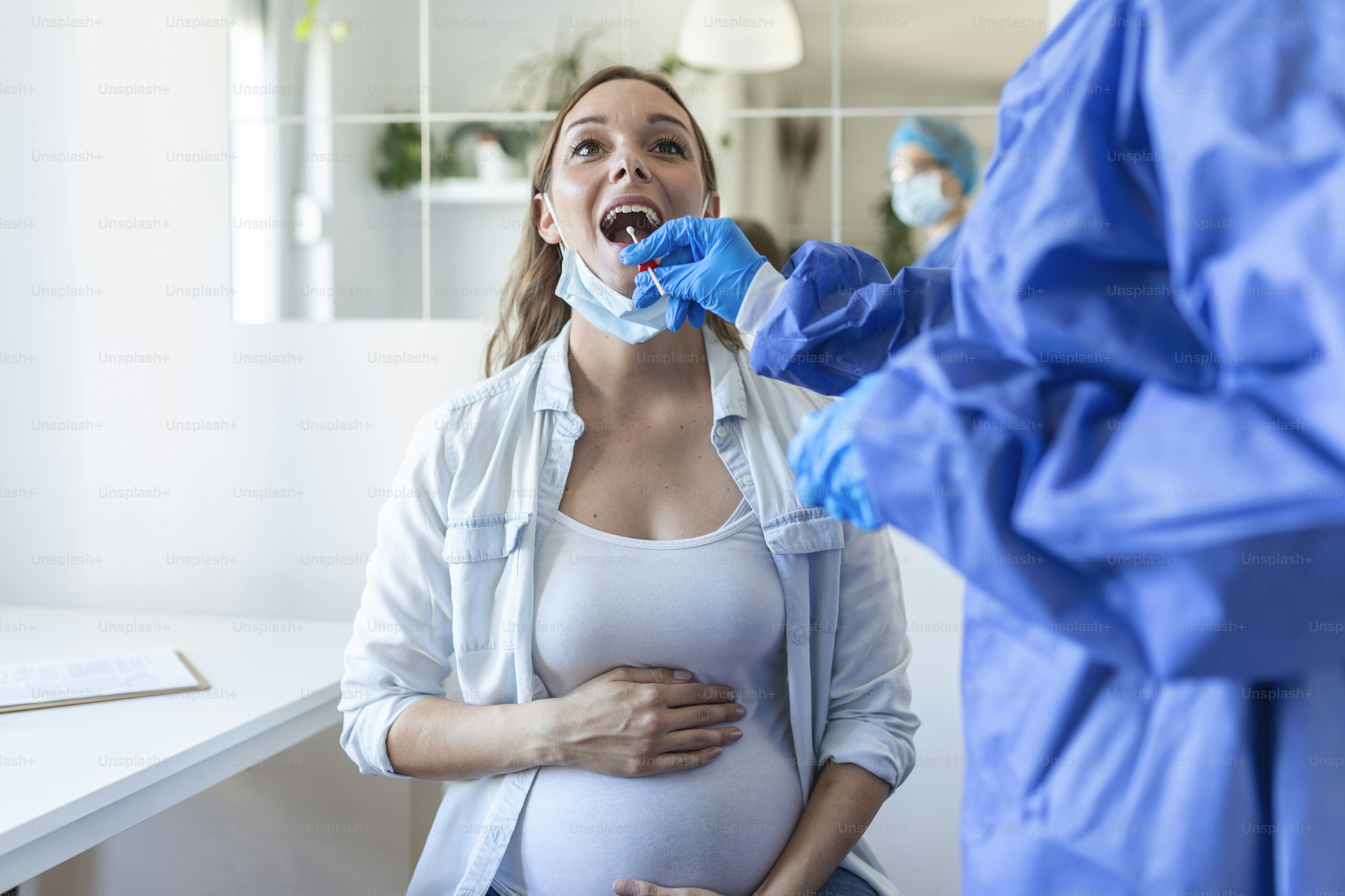 Physician wearing personal protective equipment performing a Coronavirus COVID-19 PCR test, pregnant woman nasal NP and oral OP swab sample specimen collection process, viral rt-PCR DNA procedure