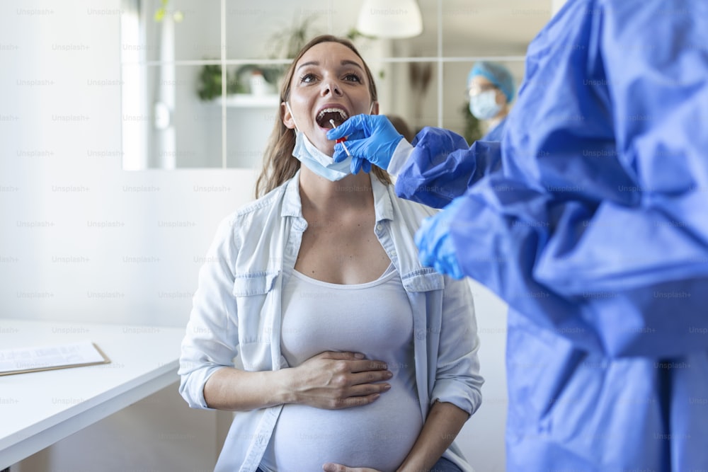 Médecin portant un équipement de protection individuelle effectuant un test PCR COVID-19 contre le coronavirus, une femme enceinte est prélevée par écouvillonnage nasal et oral OP, procédure d’ADN rt-PCR virale