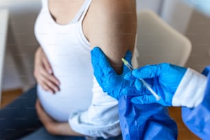 妊娠中の予防接種。妊娠中の女性にCOVID-19コロナウイルスワクチンを注射する医師。青い手袋をはめた医師が診療所で若い妊婦にワクチンを接種。人々の予防接種のコンセプト。