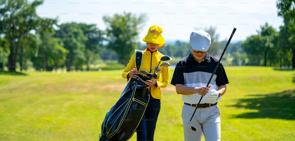 Porträt des Vertrauens Asiatischer Golfer, der Golfschläger hält und Golfball auf dem Grün des Golfplatzes an sonnigen Tagen schlägt. Gesunder Mann genießt Outdoor-Lifestyle-Aktivität Sport Golf im Country Club in den Sommerferien
