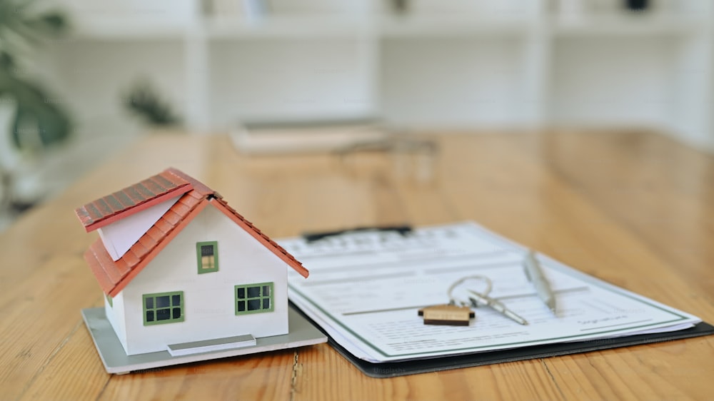 집 모델, 열쇠 및 나무 테이블에 계약 문서. 모기지 및 부동산 투자 개념.