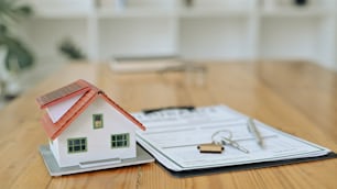 House model, keys and contract document on wooden table. Mortgage and real estate investment concept.