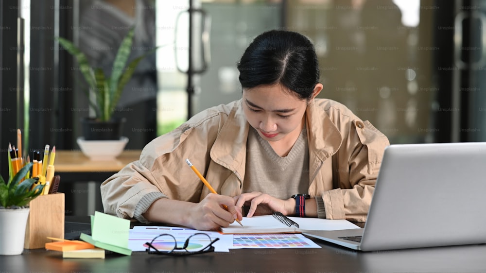 Giovane designer donna asiatica che lavora con computer portatile in ufficio.
