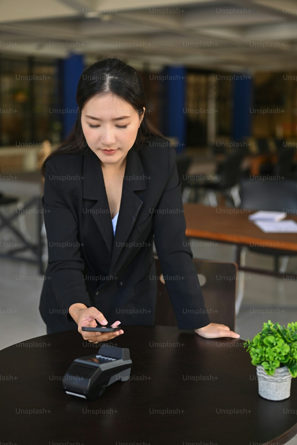 Mujer asiática sonriente usando un teléfono inteligente para el pago en la cafetería.