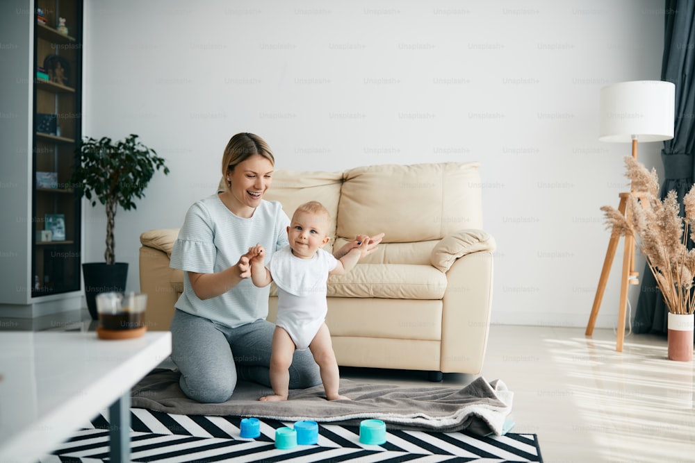 Young happy mother assisting her baby son with his first steps at home. Copy space.