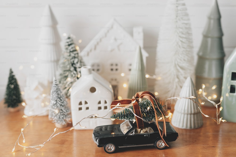 Merry Christmas and Happy New Year! Festive Christmas scene, miniature holiday village. Car with christmas tree, little houses and snowy trees on white background. Styling Christmas sideboard