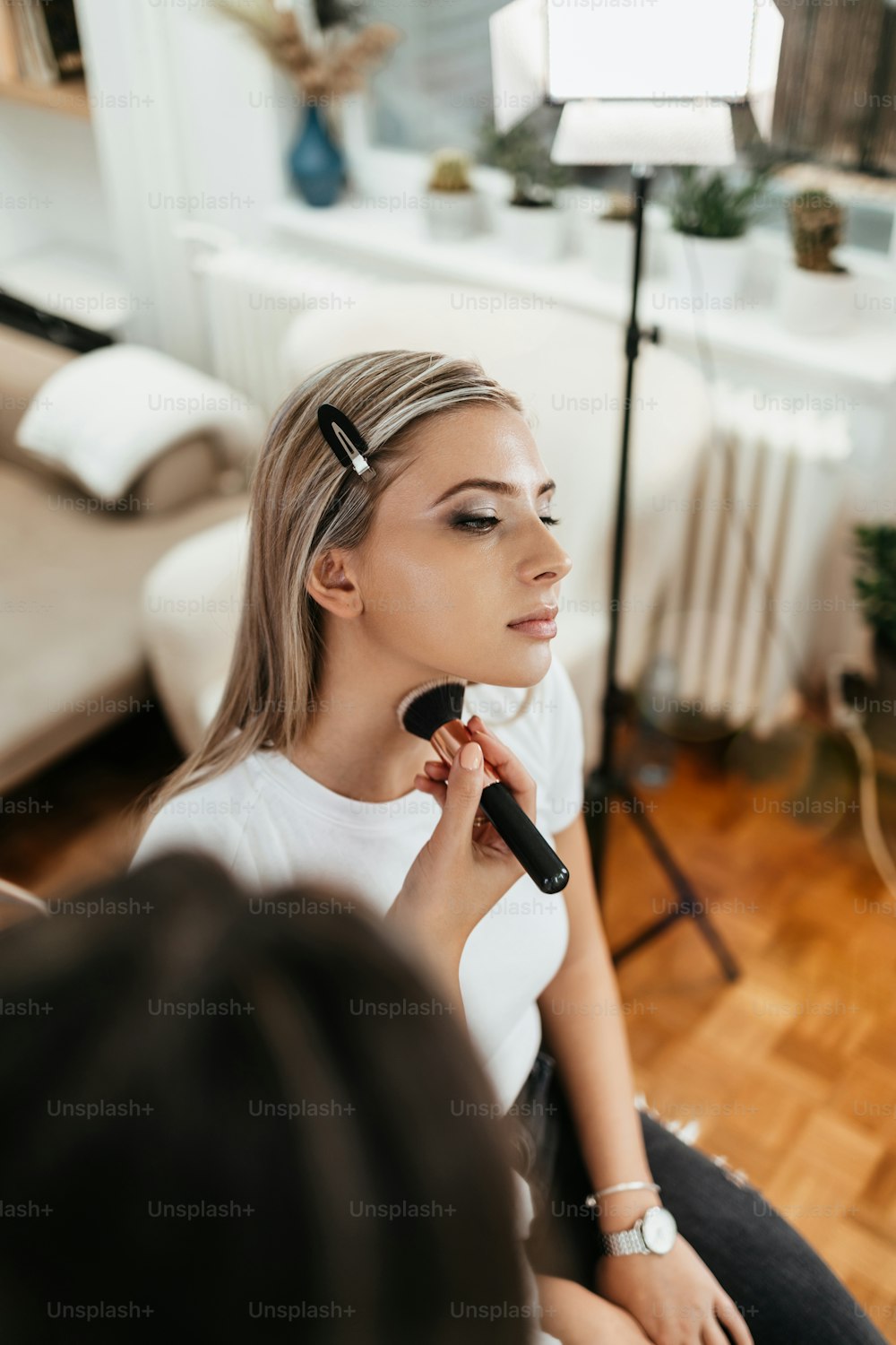 Makeup process. Professional artist applying make up on model face. Close up portrait of beautiful blonde woman in beauty saloon.