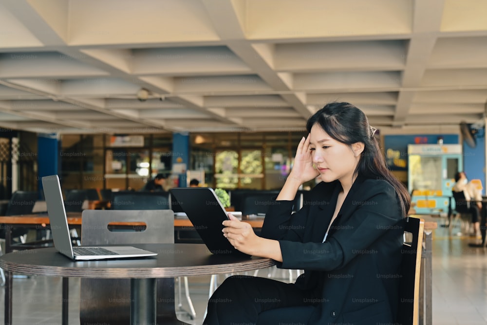 Gestresste Geschäftsfrau, die im Büro sitzt und ein digitales Tablet benutzt.
