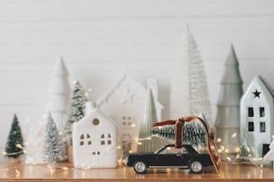 メリークリスマスと新年あけましておめでとうございます!お祝いのクリスマスシーン、ミニチュアの休日の村。 白い背景にクリスマスツリー、小さな家、雪に覆われた木々とスタイリッシュな車。クリスマスの背景