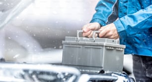 Car technician replaces dead car battery in winter conditions.