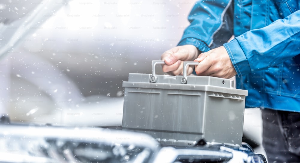 Un technicien automobile remplace la batterie de voiture déchargée dans des conditions hivernales.
