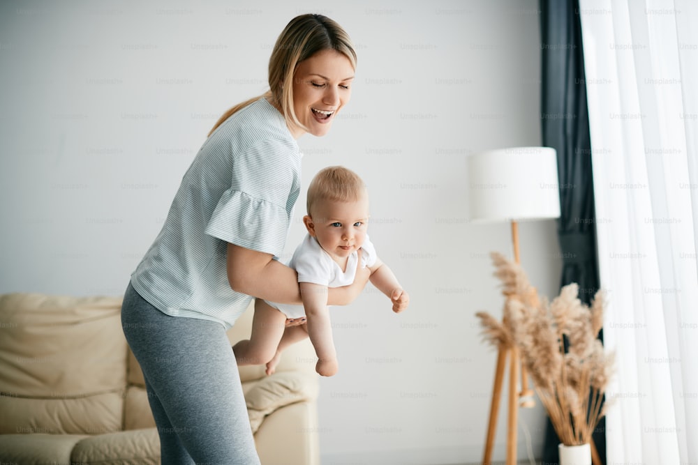 Young mother having fun while playing with her baby son in the living room. Copy space.