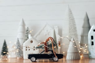 Holidays coming! Festive Christmas scene, miniature holiday village. Car with christmas tree, little houses and snowy trees on white background. Merry Christmas and Happy New Year !