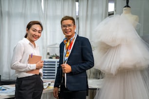 Ritratto di sorridente ragazzo asiatico LGBTQ proprietario di un negozio di abiti da sposa che lavora insieme all'assistente femminile nella stanza dell'ufficio presso lo studio di nozze. Piccola impresa, imprenditrice, wedding planner e designer concept