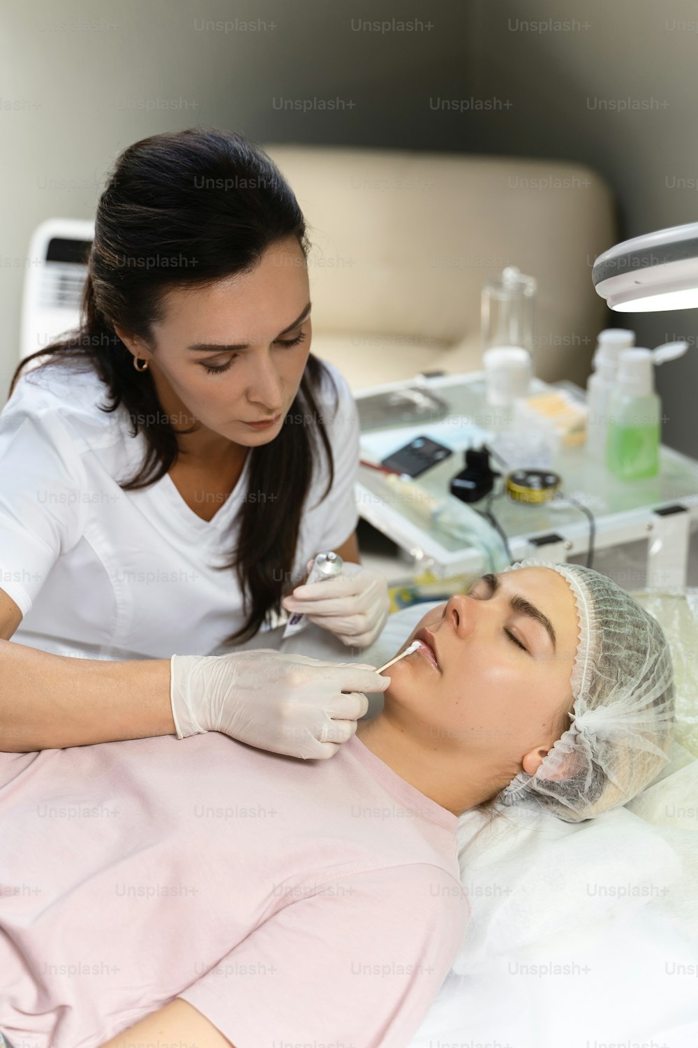 Professional permanent make-up artist applying anesthetic on client's lips before lip blushing procedure