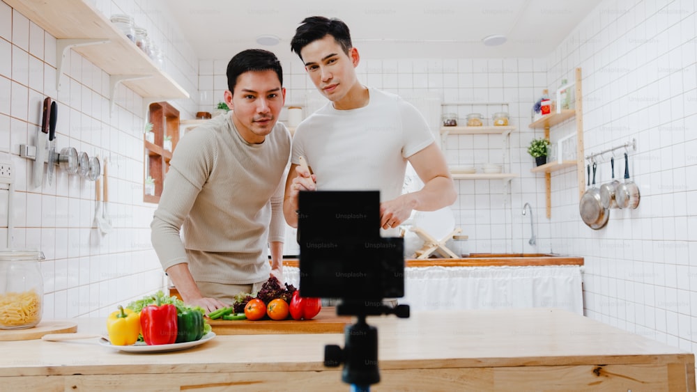 Asia gay couple blogger vlogger and online influencer recording video content on healthy food in kitchen at home.