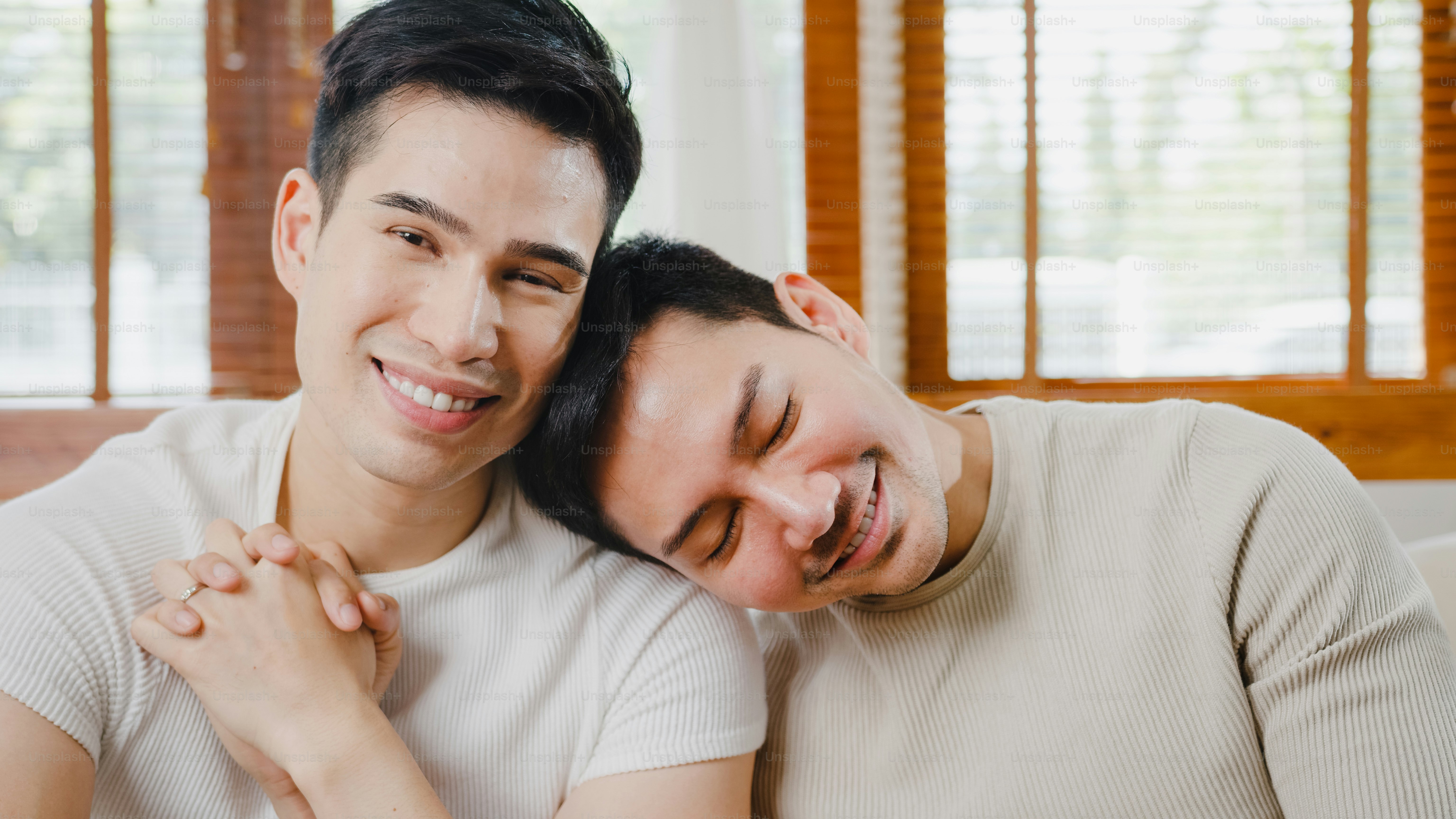 Portrait Young Asia Gay couple feeling happy showing ring at home. Asia LGBTQ+ men relax toothy smile looking to camera while hug in modern living room at house in the morning concept.