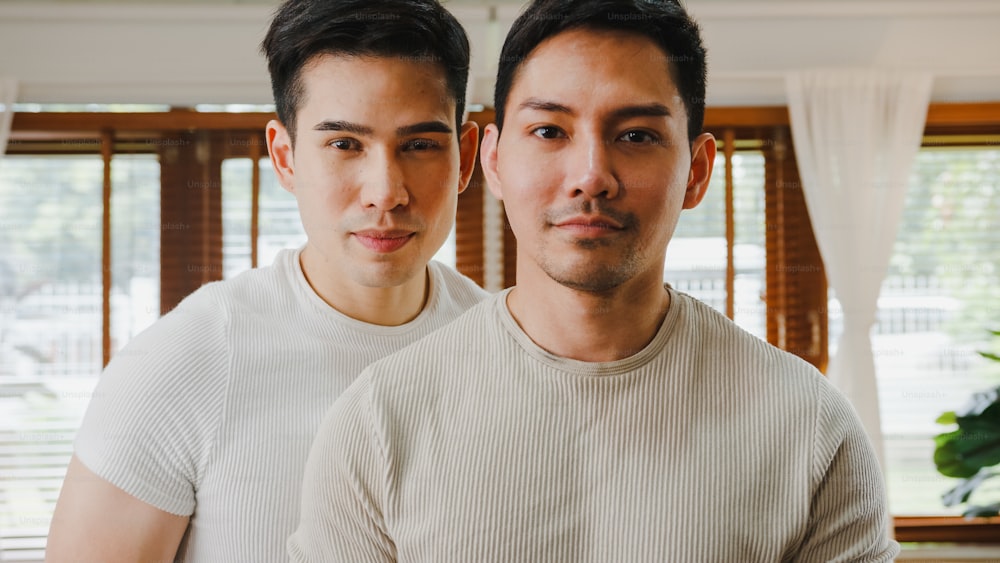 Portrait Young Asia Gay couple feeling happy smiling at home. Asian LGBTQ men relax toothy smile looking to camera while hug in living room at home.
