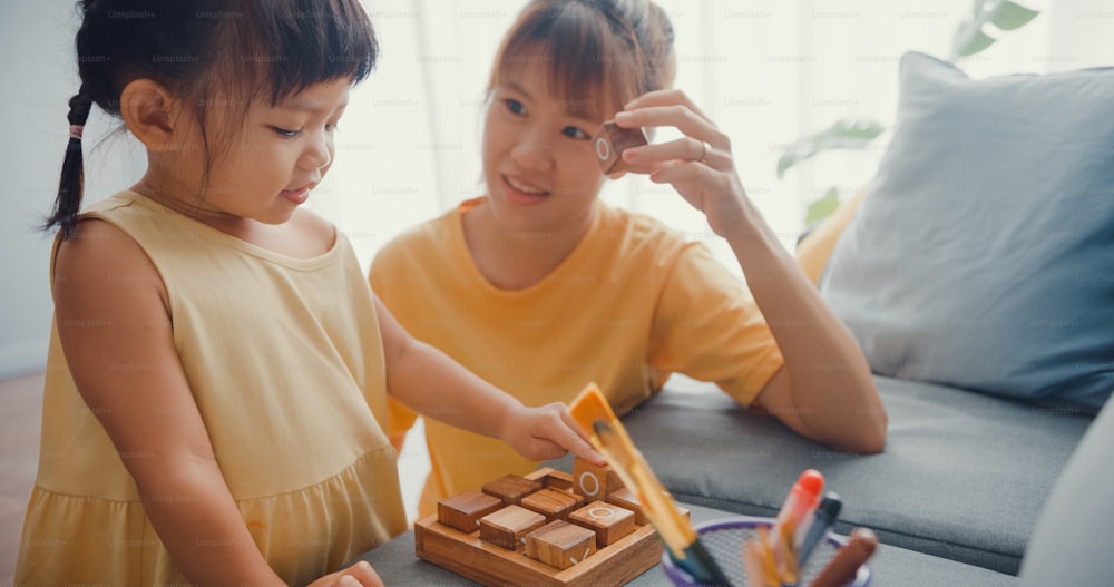 Happy Asia family mom teach girl play board game hobby with wooden box having fun relax on couch in living room at house. Spending time together, Social distance, Quarantine for coronavirus.