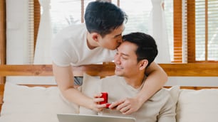Joven pareja gay asiática propone matrimonio en casa moderna, los hombres LGBTQ felices sonriendo tienen un momento romántico mientras proponen matrimonio y la sorpresa del matrimonio usan un anillo de bodas en la sala de estar de la casa.
