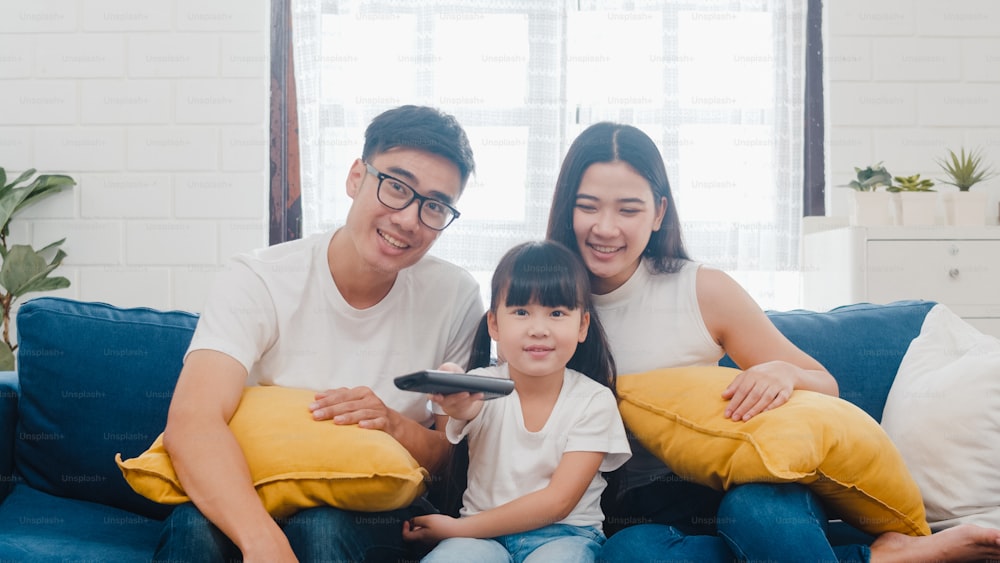 Estilo de vida coreano pai, mãe e filha assistindo TV juntos e se divertindo deitado no sofá na sala de estar na casa moderna.