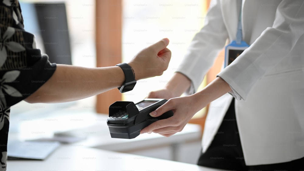 Imagem recortada em close-up de um homem usando seu moderno relógio de pulso digital pagando suas compras. Tecnologia NFC, sociedade sem dinheiro, distanciamento social.