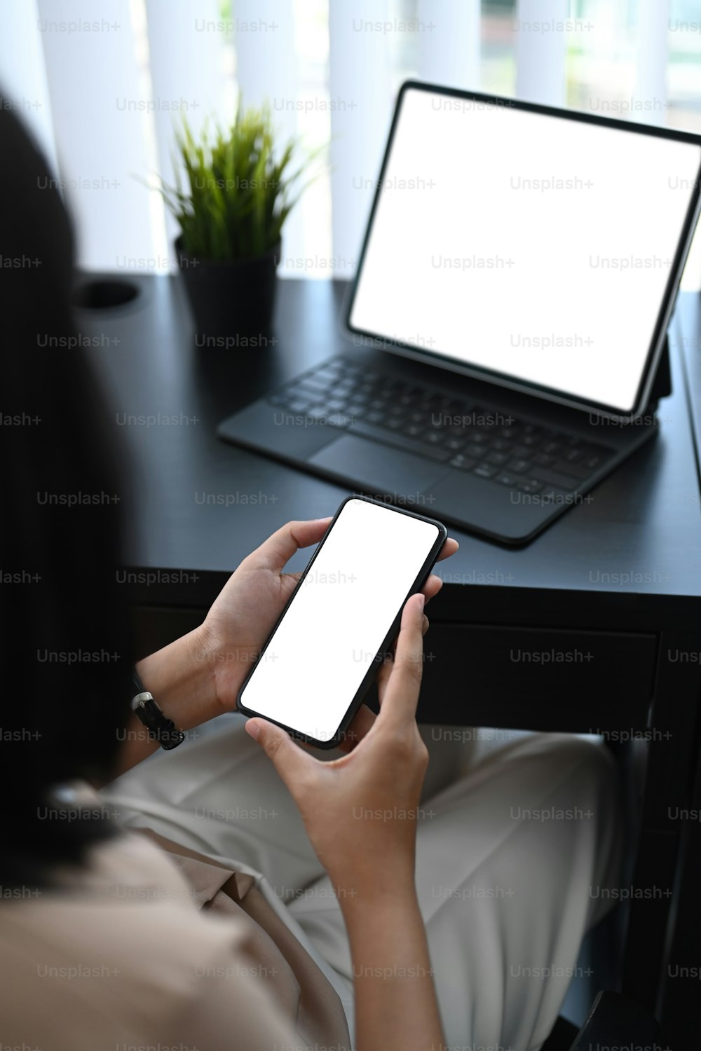 Vista sobre el hombro de una mujer de negocios sentada en una oficina moderna y usando un teléfono inteligente.